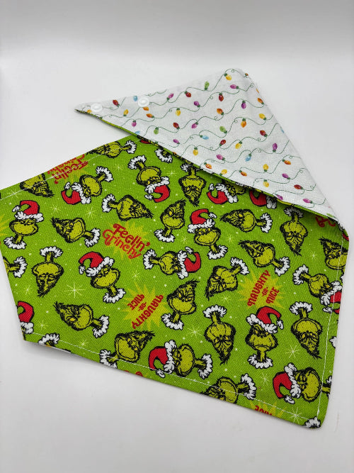 Green dog bandana featuring Grinch wearing Santa hat and catchy sayings and reversible pattern with Christmas lights on white background.