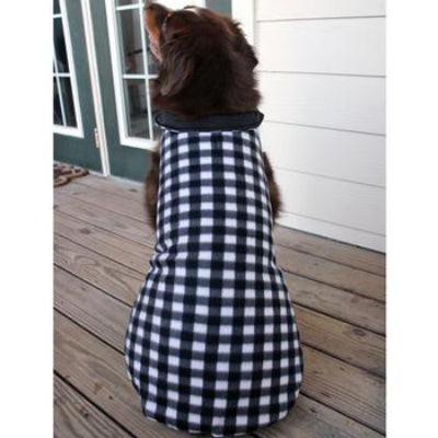 Dog wearing a black and white checkered coat on a wooden deck.