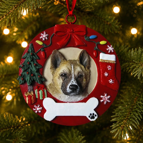 A round red Christmas ornament hanging on a Christmas tree, featuring a custom photo of an Akita in the center surrounded by festive decorations including a tree, stocking, bone, and gifts.