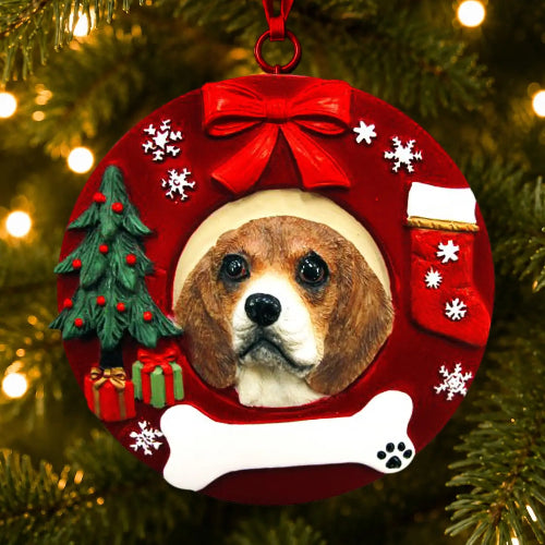 A personalized Christmas ornament shaped like a red holiday wreath, hanging on a Christmas tree. The ornament features a custom photo cutout of a Cavalier King Charles Spaniel dog's face, surrounded by festive decorations including a red bow, white snowflakes, a small green Christmas tree, a red stocking, a bone, and a gift box.