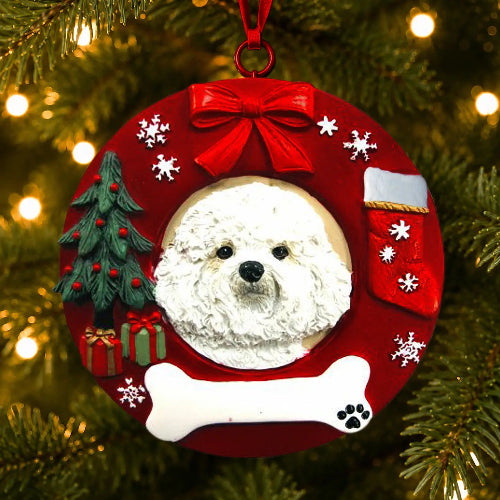 A round red Christmas ornament hanging on a lit Christmas tree. The ornament features a white Bichon Frise dog portrait in the center, surrounded by a red bow, white snowflakes, a green Christmas tree, a red stocking, a white bone, and a small gift box.