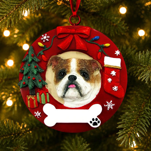 A personalized Christmas ornament shaped like a red wreath with a custom bulldog portrait in the center, hanging on a Christmas tree with lights. The ornament features a red bow, a decorated tree, a stocking, a white bone, and snowflake details.