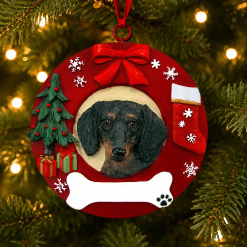 A circular red Christmas ornament featuring a custom photo of a dachshund, decorated with a red bow, white snowflakes, a small green Christmas tree, a red stocking, a white bone, and a paw print, hanging on a lit Christmas tree.