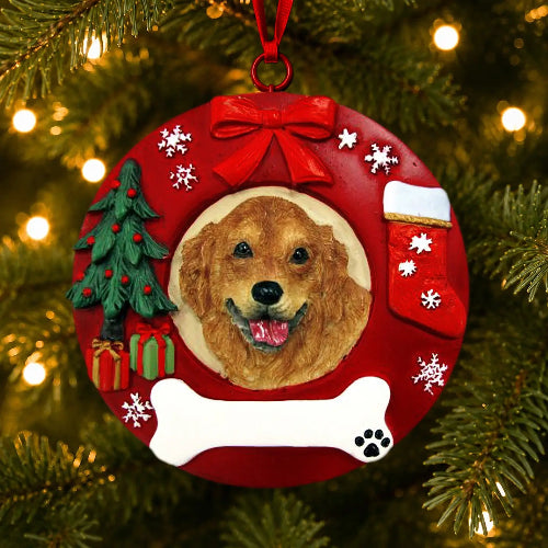 A round red Christmas ornament hanging on a lit Christmas tree. The ornament features a custom pet portrait of a golden retriever in the center, surrounded by holiday decorations including a red bow, white snowflakes, a small green Christmas tree, a red stocking, a white bone, and a red hanging ribbon.