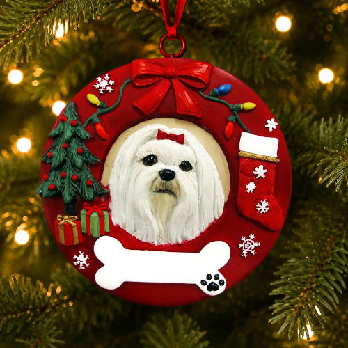A circular red Christmas ornament hanging on a Christmas tree, featuring a portrait of a Maltese, a red bow, a small green tree, a stocking, lights, snowflakes, and a white bone-shaped plaque at the bottom.