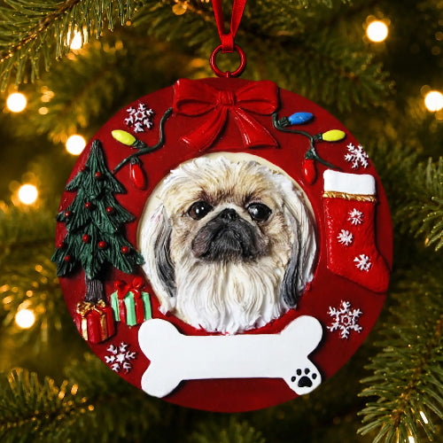 A round Christmas ornament featuring a portrait of a Pekignese, decorated with a red bow, stocking, bone, tree, and gifts, hanging on a Christmas tree with warm lights.