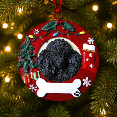 A round red Christmas ornament hanging on a Christmas tree, featuring a black poodle in the center, surrounded by holiday decorations including a green tree, stockings, snowflakes, lights, and a white bone at the bottom.