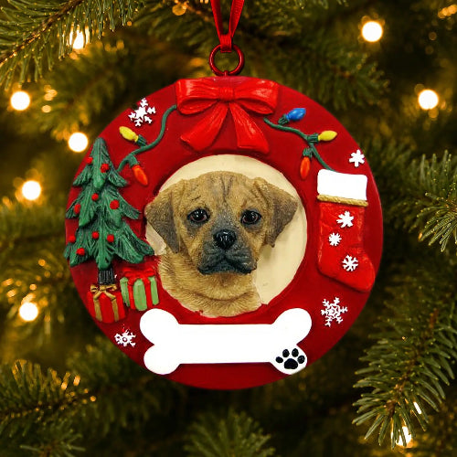 A red circular Christmas ornament hanging on a Christmas tree, featuring a custom photo of a Puggle in the center, surrounded by festive decorations including a green Christmas tree, red bow, stockings, and a white bone at the bottom.