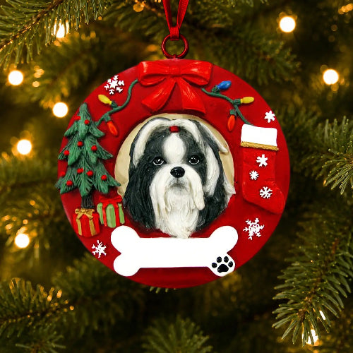 A circular red Christmas ornament hanging on a lit Christmas tree. The ornament features a portrait of a black-and-white Shih Tzu in the center, surrounded by holiday decorations including a small tree, gifts, snowflakes, a bone shape, and a red bow at the top.