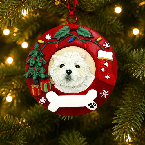 A red Christmas wreath-shaped pet ornament hanging on a Christmas tree. The ornament features a raised West Highland White Terrier in the center, surrounded by holiday decorations including a green Christmas tree, red stockings, gift boxes, holly, colorful lights, snowflakes, and a white bone at the bottom.