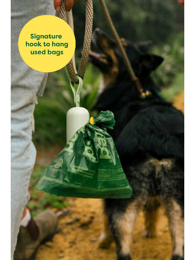 Green dog waste bag hanging from a hook with a yellow label, blurred background