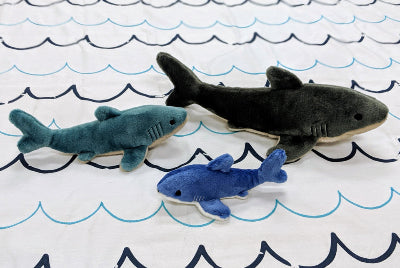 Three shark-shaped dog toys on a fabric surface with wavy patterns.