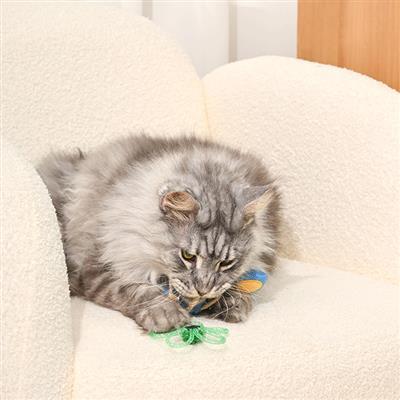 Cat playing with a green toy on a white cushion