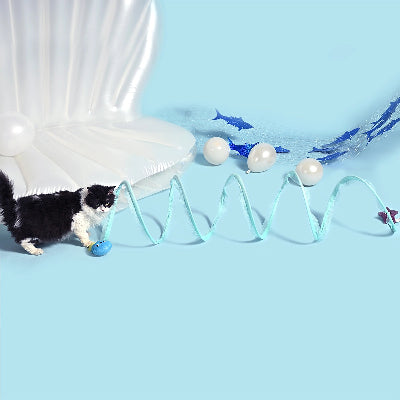 Cat playing with a toy track set up on a blue surface with fish and pearl-like objects.