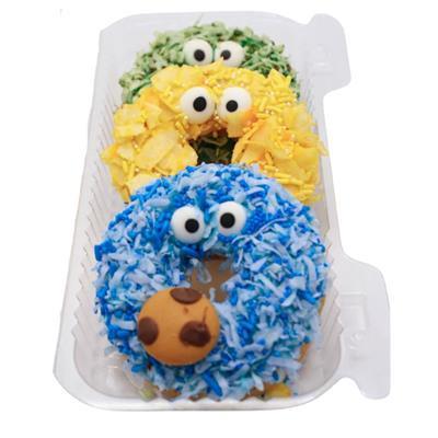 Three cookie-shaped cakes, one blue, one yellow and one green, with eyes and a mouth on a white background.