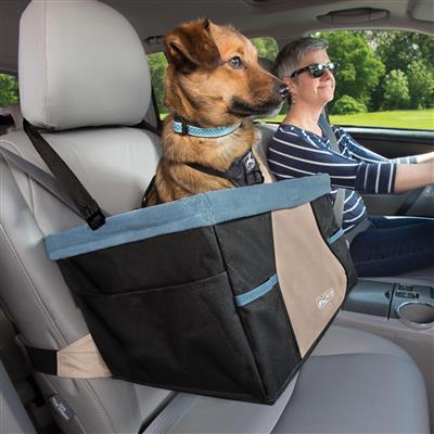 Dog in a car seat cover with a person driving, surrounded by greenery outside.