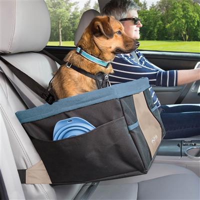 Dog in a car seat cover with a person driving, surrounded by greenery outside.