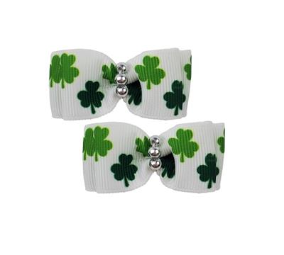 Two white hair bows with green shamrock patterns and silver beads on a white background