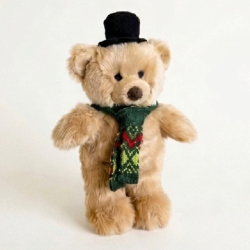 Bear dog toy wearing green scarf and black top hat on white background.