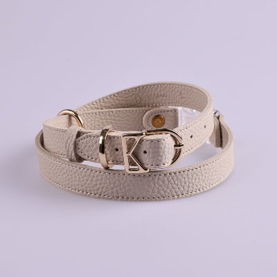 Beige leather dog harness with gold buckle on a light purple background