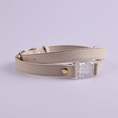 Beige leather dog harness with clear plastic buckle on a light gray background