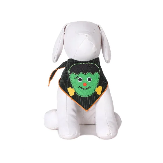 A white plush dog toy wearing a black pinstriped bandana with a green Frankenstein monster face and yellow lightning accents, photographed on a white background.