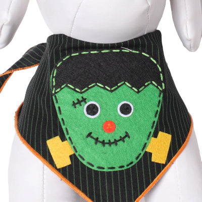 A Halloween-themed  bandana bib displayed on a white mannequin torso. The bib features a green felt Frankenstein face with black hair, yellow lightning bolts, and an orange nose, set against a black pinstriped fabric with an orange border.