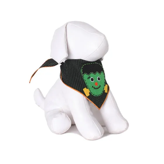 A white plush dog toy wearing a black pinstriped bandana with a green Frankenstein monster face design and orange trim, photographed on a clean white background.