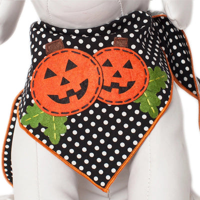 A Halloween-themed pet bandana bib with a black and white polka dot pattern, featuring two orange felt jack-o'-lantern faces and green felt leaves, displayed on a white mannequin.