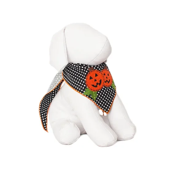 A white plush dog toy wearing a black and white polka dot bandana with orange embroidered pumpkins and green leaves, set against a plain white background.