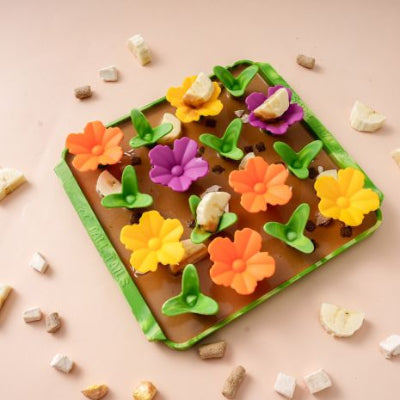 Flower-shaped foraging mat for pets on a pink background with scattered ingredients