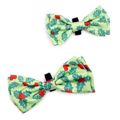 Two green bow ties with red berries and black clips on a white background