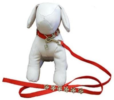 White dog mannequin wearing red collar attached to red leash with silver metal flowers on white background.